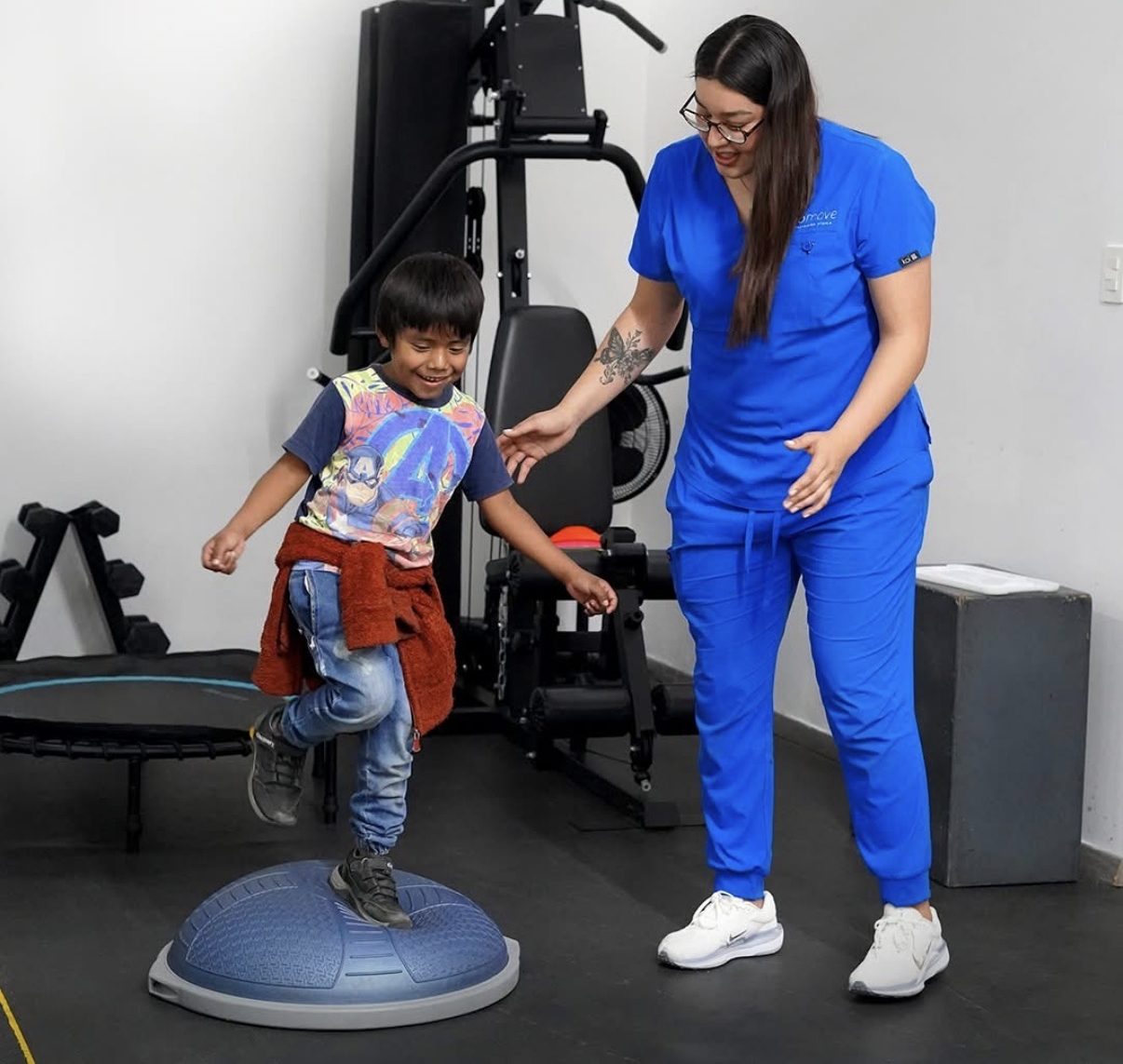 Fisioterapeuta guiando a un niño en ejercicio de equilibrio sobre medio balón