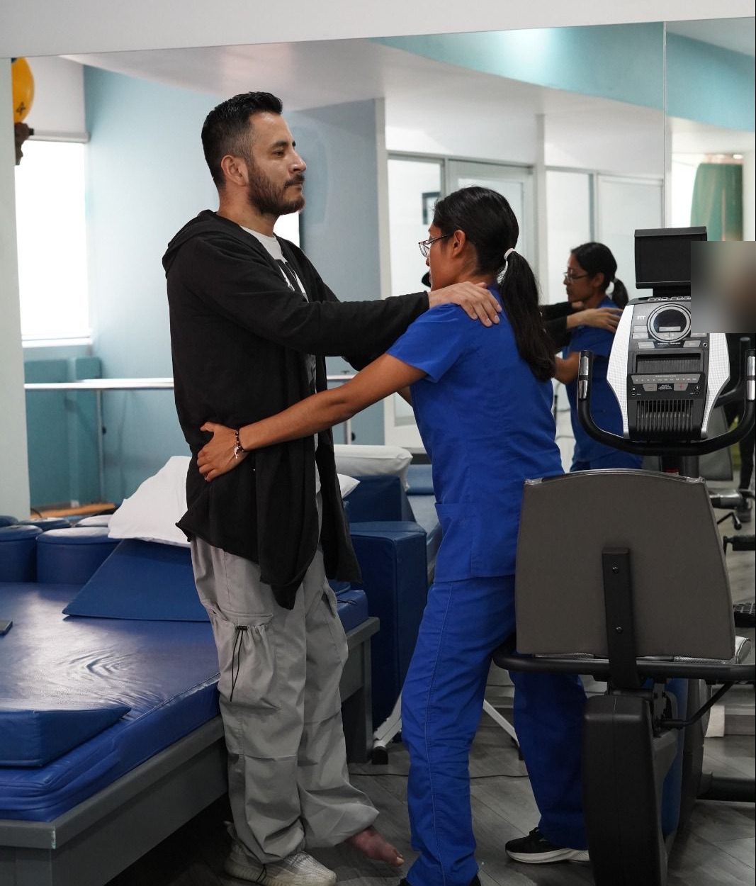 Fisioterapeuta dando apoyo a un paciente de pie durante un ejercicio de equilibrio