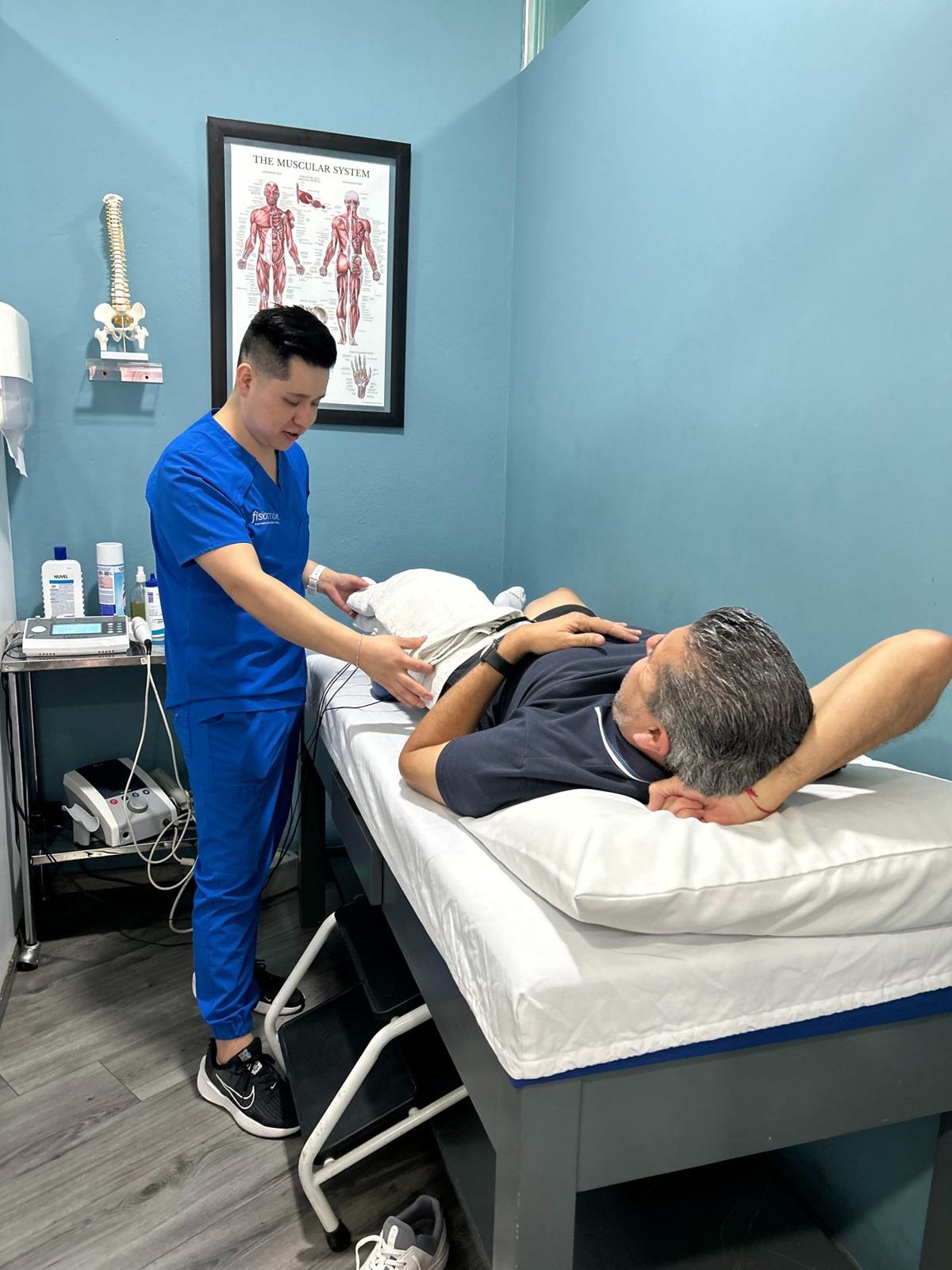 Fisioterapeuta colocando compresa y electroterapia a un paciente en la camilla